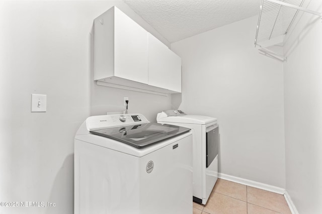 laundry area featuring cabinet space, light tile patterned floors, baseboards, washer and clothes dryer, and a textured ceiling