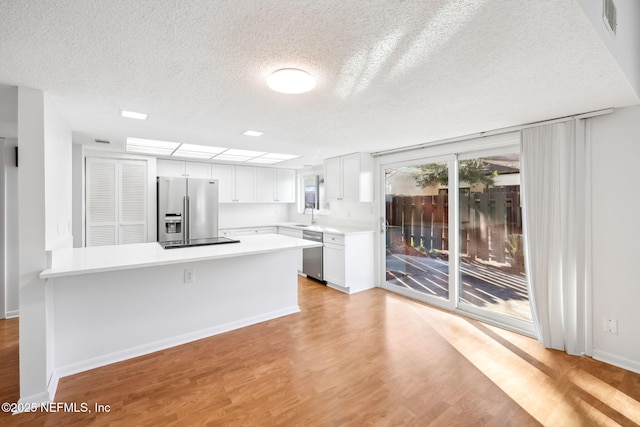 kitchen featuring stainless steel appliances, light countertops, light wood-style floors, white cabinetry, and a peninsula