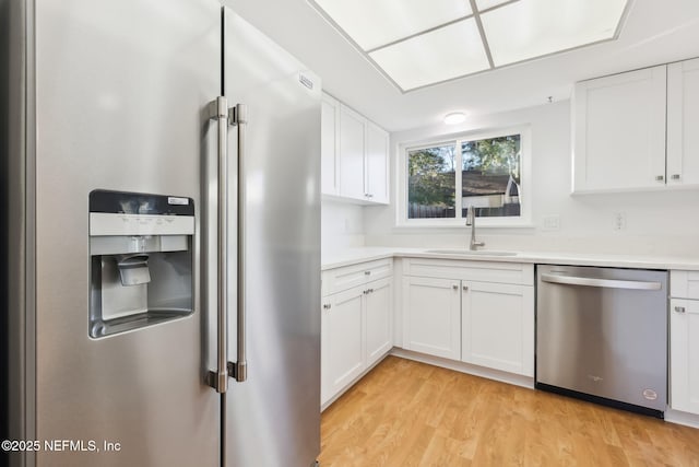 kitchen with light wood-style flooring, stainless steel appliances, light countertops, white cabinetry, and a sink