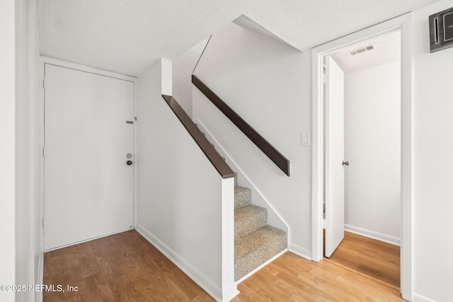 stairway with baseboards, a textured ceiling, visible vents, and wood finished floors