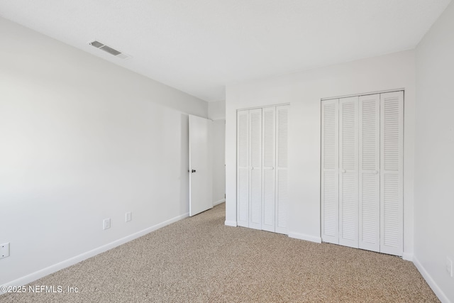 unfurnished bedroom featuring baseboards, carpet flooring, visible vents, and multiple closets