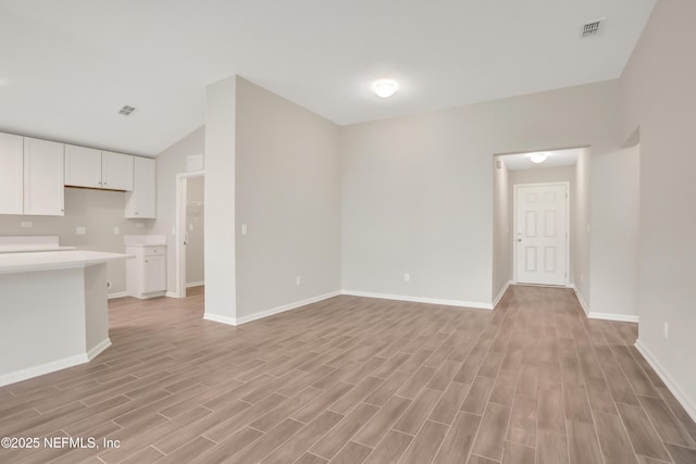 unfurnished living room with visible vents, vaulted ceiling, light wood-style flooring, and baseboards