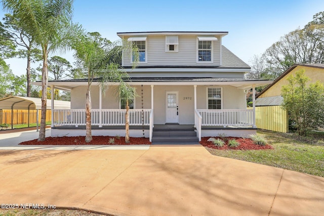 view of front of house with a porch, a detached carport, driveway, and fence