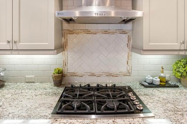 kitchen with decorative backsplash, white cabinetry, light stone countertops, stovetop, and wall chimney exhaust hood