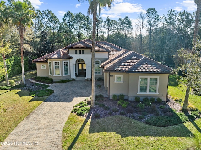 mediterranean / spanish-style house with decorative driveway, a tile roof, a front lawn, and stucco siding