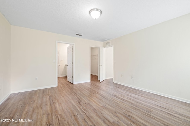 unfurnished bedroom with a closet, visible vents, a spacious closet, light wood-type flooring, and baseboards