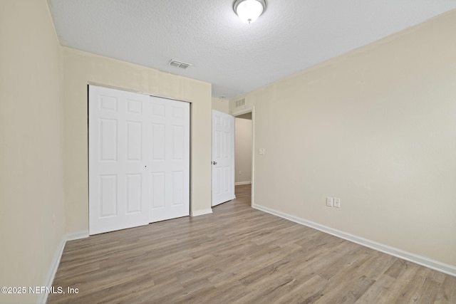 unfurnished bedroom with a closet, a textured ceiling, baseboards, and wood finished floors