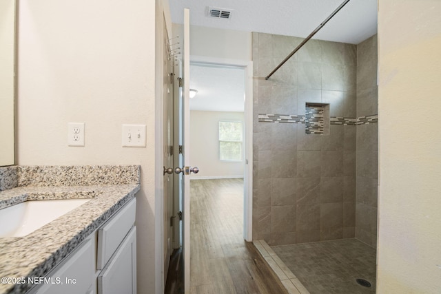 bathroom with wood finished floors, visible vents, vanity, and tiled shower