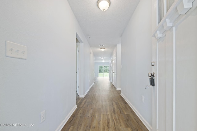 corridor with a textured ceiling, baseboards, and wood finished floors