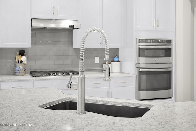 kitchen featuring stainless steel appliances, decorative backsplash, white cabinets, a sink, and under cabinet range hood