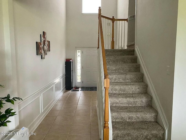 tiled entrance foyer with wainscoting, a decorative wall, a towering ceiling, and stairs