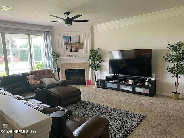 carpeted living area featuring baseboards, visible vents, a ceiling fan, a tile fireplace, and ornamental molding