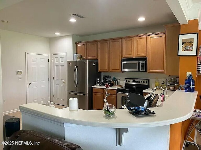 kitchen with a peninsula, a kitchen bar, stainless steel appliances, and light countertops