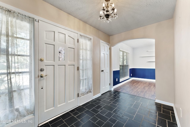 foyer featuring baseboards, a notable chandelier, arched walkways, and a textured ceiling