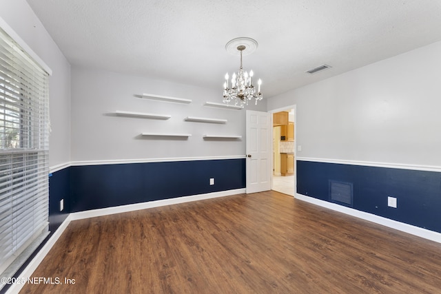 unfurnished room featuring visible vents, a textured ceiling, an inviting chandelier, and wood finished floors