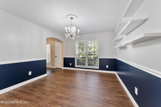 interior space featuring arched walkways, baseboards, wood finished floors, and an inviting chandelier