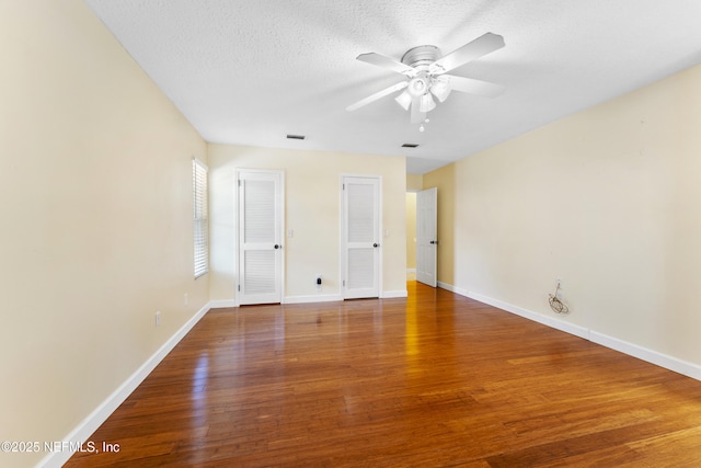 unfurnished bedroom featuring visible vents, a textured ceiling, baseboards, and wood finished floors