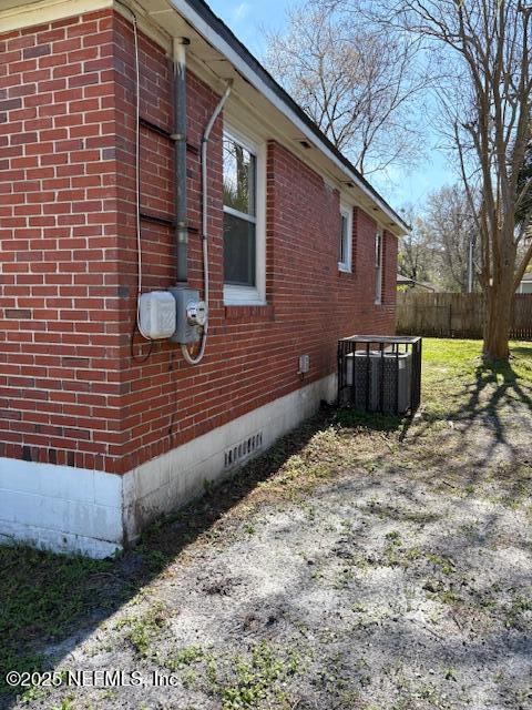 view of property exterior with crawl space, brick siding, fence, and central AC