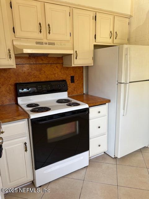 kitchen with light tile patterned floors, under cabinet range hood, electric range, backsplash, and freestanding refrigerator