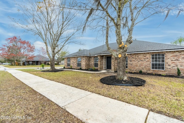 view of front of house featuring a front yard, brick siding, and roof with shingles