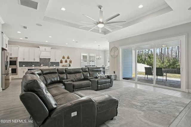 living room with light wood-type flooring, visible vents, a tray ceiling, and ornamental molding