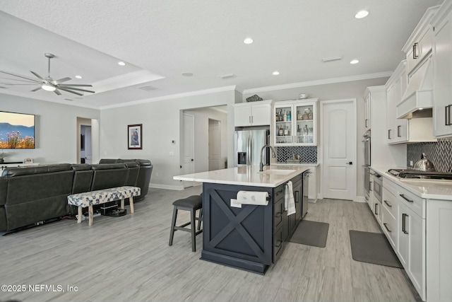 kitchen with stainless steel appliances, light countertops, open floor plan, white cabinetry, and a sink