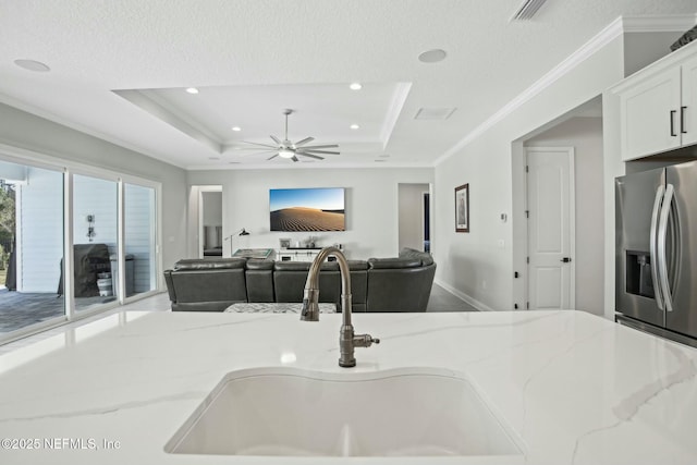 kitchen with a sink, stainless steel refrigerator with ice dispenser, light stone countertops, a tray ceiling, and crown molding