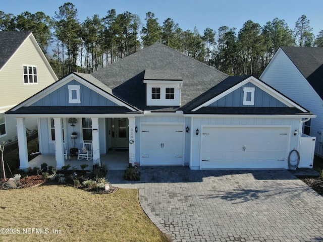 view of front of house with board and batten siding, covered porch, decorative driveway, and an attached garage