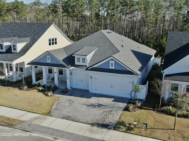 view of front of property featuring covered porch, a garage, roof with shingles, decorative driveway, and board and batten siding