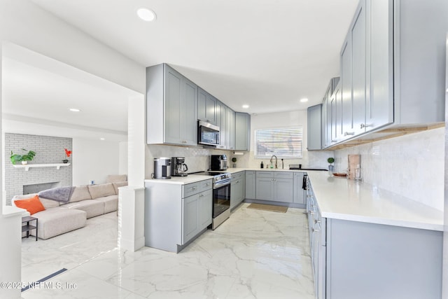 kitchen featuring gray cabinetry, a fireplace, a sink, marble finish floor, and appliances with stainless steel finishes