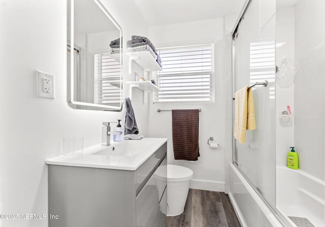 bathroom with bath / shower combo with glass door, toilet, vanity, wood finished floors, and baseboards