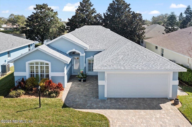 ranch-style house featuring cooling unit, roof with shingles, decorative driveway, stucco siding, and a front lawn