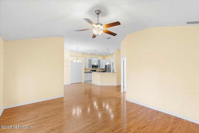 unfurnished living room with visible vents, baseboards, light wood-style flooring, vaulted ceiling, and ceiling fan with notable chandelier