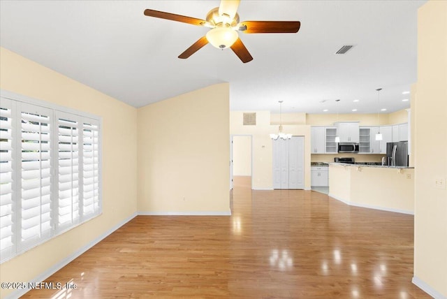 unfurnished living room featuring ceiling fan with notable chandelier, light wood-style flooring, visible vents, and baseboards