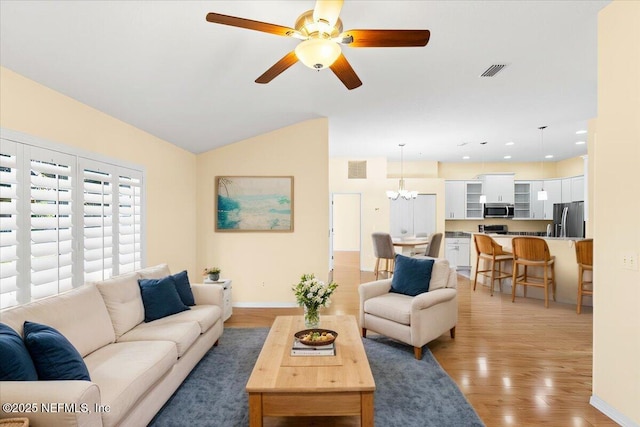 living room featuring visible vents, light wood-style floors, vaulted ceiling, baseboards, and ceiling fan with notable chandelier