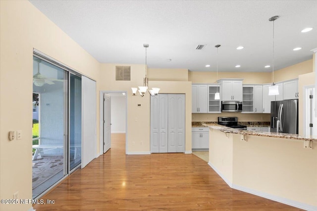 kitchen featuring light wood finished floors, visible vents, glass insert cabinets, a breakfast bar area, and stainless steel appliances