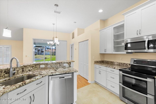 kitchen featuring white cabinets, appliances with stainless steel finishes, light stone countertops, pendant lighting, and a sink