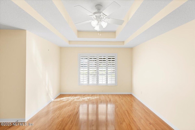 unfurnished room with baseboards, a raised ceiling, and wood finished floors