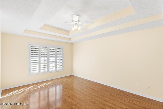 spare room featuring a textured ceiling, ceiling fan, wood finished floors, baseboards, and a raised ceiling