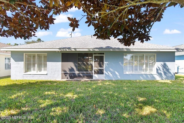 rear view of property featuring a shingled roof, a lawn, and stucco siding