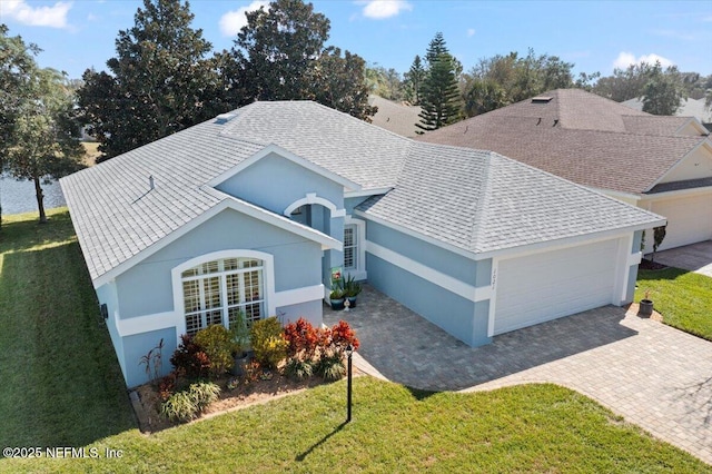 view of front of property featuring an attached garage, a shingled roof, decorative driveway, stucco siding, and a front yard