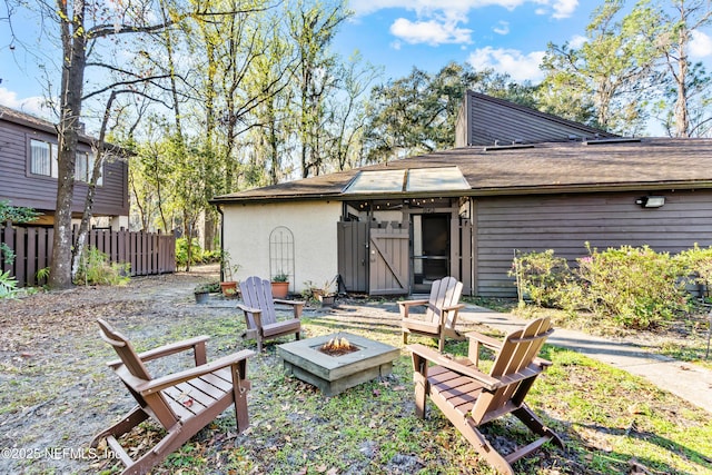 back of property featuring an outdoor fire pit, fence, and stucco siding