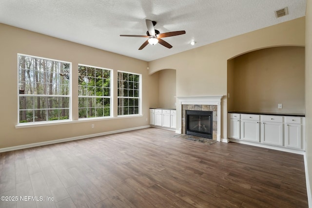 unfurnished living room featuring visible vents, a tile fireplace, ceiling fan, wood finished floors, and a textured ceiling