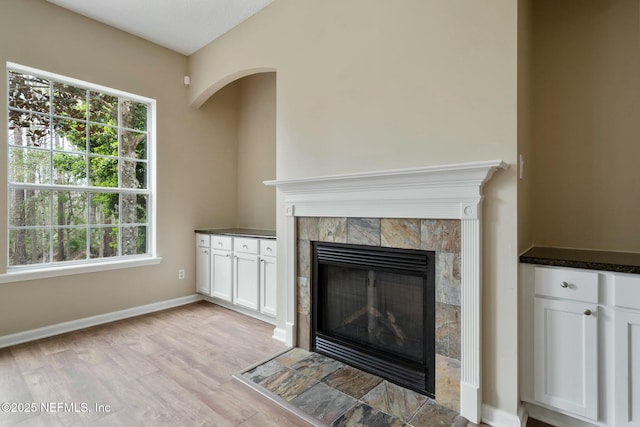 unfurnished living room featuring light wood-type flooring, a tiled fireplace, and baseboards