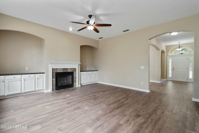 unfurnished living room with a textured ceiling, a fireplace, wood finished floors, visible vents, and baseboards