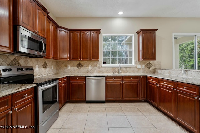 kitchen featuring light tile patterned floors, decorative backsplash, appliances with stainless steel finishes, light stone countertops, and a sink