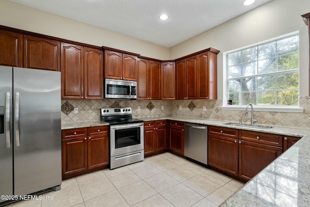 kitchen with decorative backsplash, appliances with stainless steel finishes, light stone counters, and a sink