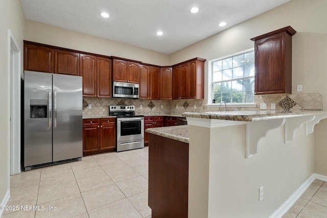 kitchen featuring appliances with stainless steel finishes, tasteful backsplash, a peninsula, and light tile patterned floors