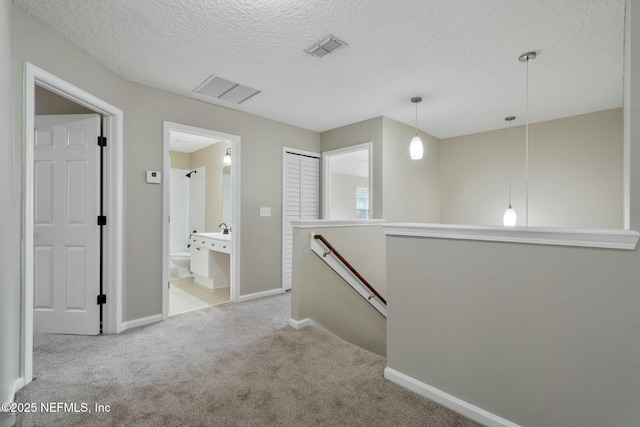 hallway with a textured ceiling, visible vents, carpet flooring, and an upstairs landing