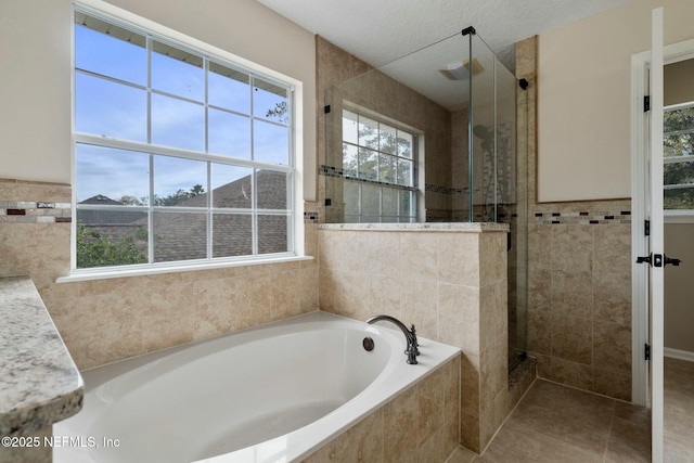 full bath with tile patterned floors, a garden tub, a textured ceiling, a shower stall, and tile walls